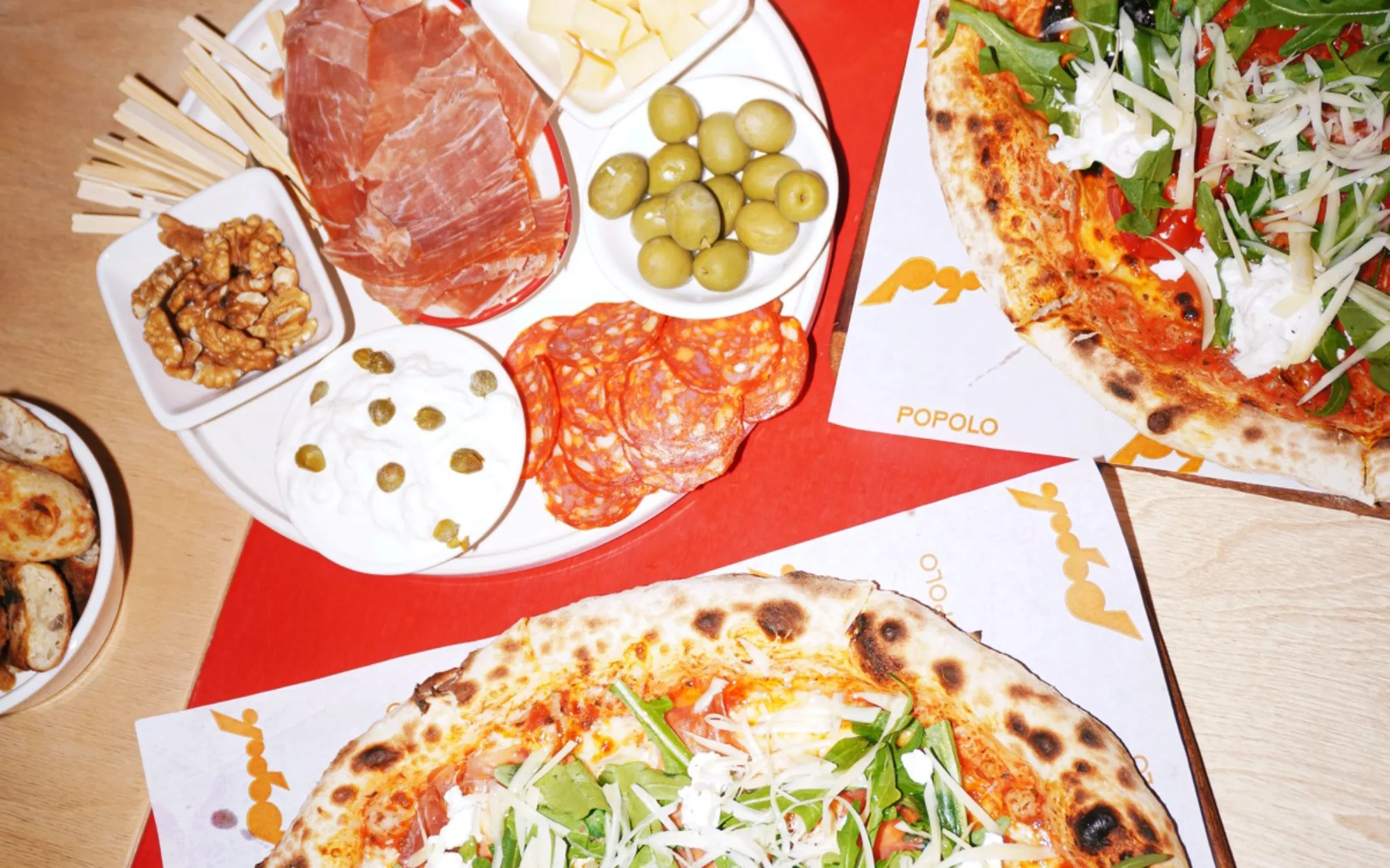 Wood-fired pizzas and an antipasti board on Popolo paper, from above